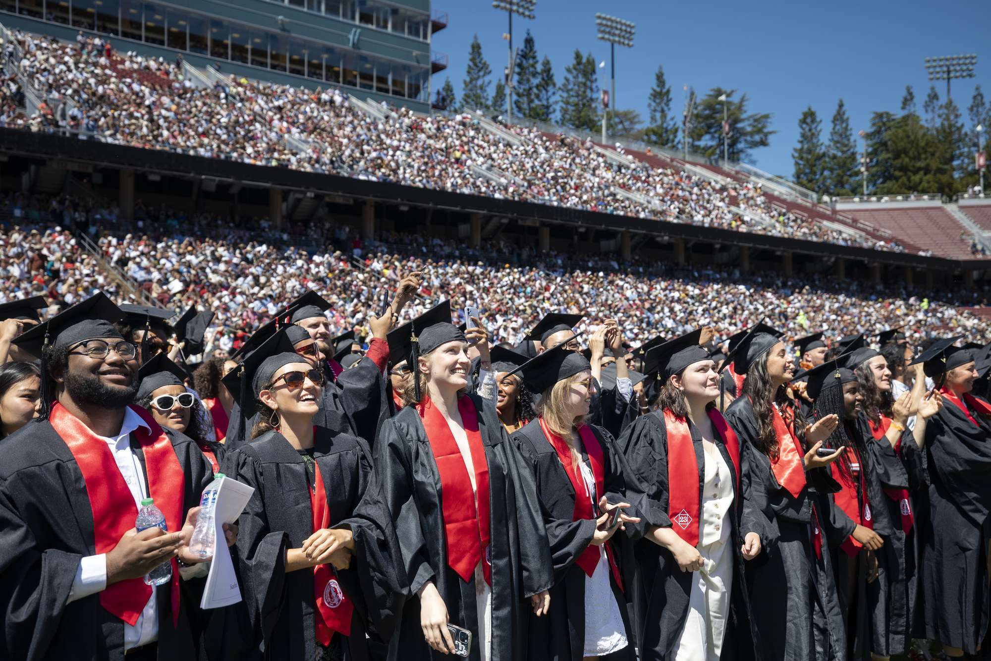 Graduates stand in cap and gown in the football stadium